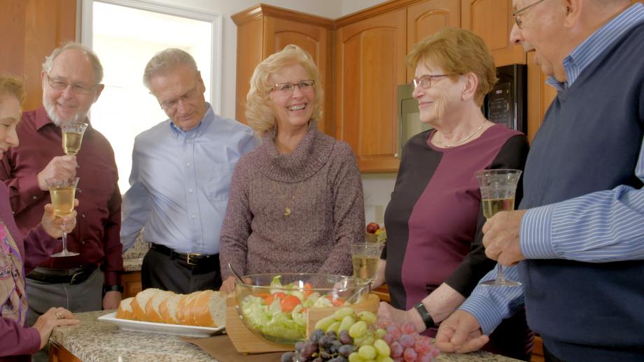 Older friends gathered in a kitchen around a food spread